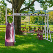 This image shows the Honey Bear Hangout Vinyl swing set with three swing positions and a slide