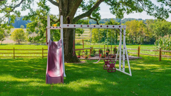 This image shows the Honey Bear Hangout Vinyl swing set with three swing positions and a slide