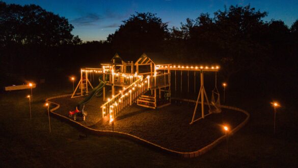 This image shows a swing set lit up at night with string lights. Click here to learn how to take your swing set to the next level.