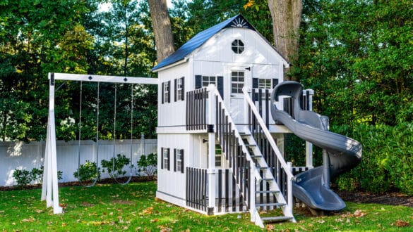 This image shows a white swing set playhouse nestled in backyard.