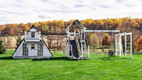 This image shows a white and black A-frame playhouse connected to a playground from King Swings.