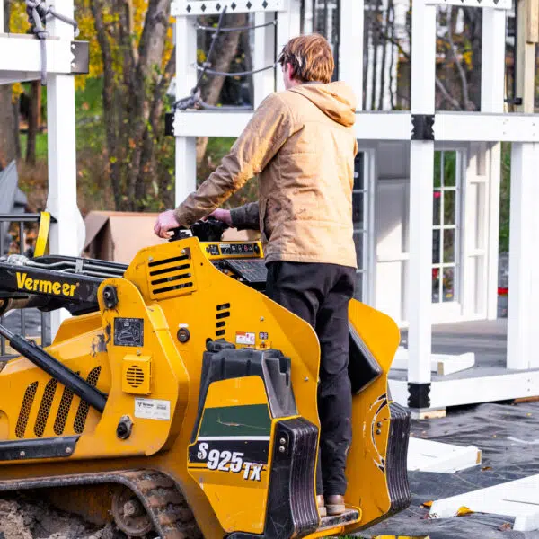 This image shows a King Swings install crew member operating a mini skid steer to install a playhouse.