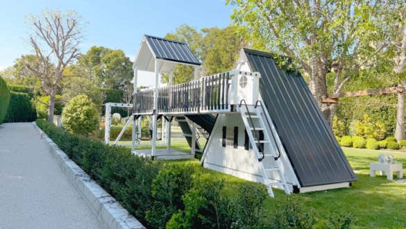 the back view of a white a frame playhouse swing set in a backyard