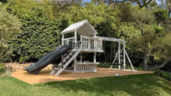 A white swing set with gray slides in backyard