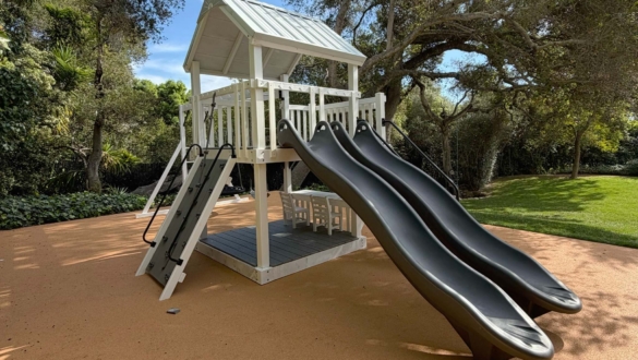A white swing set with gray slides in backyard